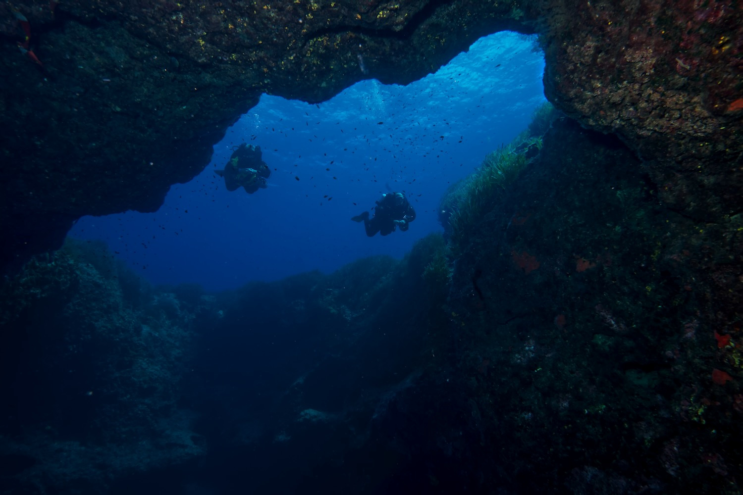 Rock arch with with two divers swimming through it