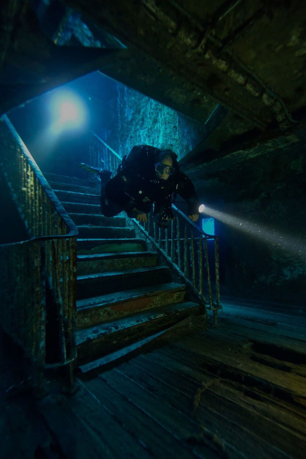 Diver on a wreck staircase with torch beam
